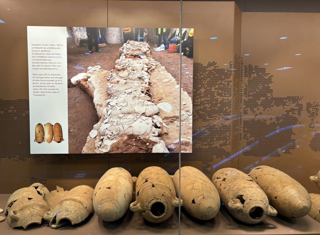 Gaza-style amphorae from the Byzantine-period storehouses discovered at Dimokratias station, displayed reconstructed in a museum display case, with a photo above showing the original destroyed amphorae in situ. Photo courtesy Mark Wilson