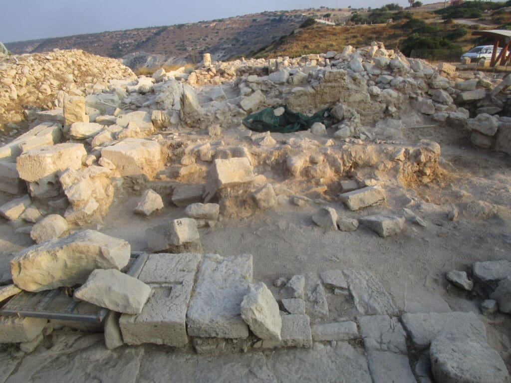 A surface dig site situated on hilly countryside, showing stone blocks strewn about, plus some foundation stones in place. Kourion Urban Space Project, courtesy Thomas Davis