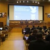 People sitting in seats in front of a projection screen in a large room. Courtesy UNESCO