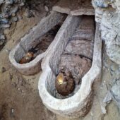 two wooden coffins with mummies inside wrapped in cloths with geometric shapes and with gold on the skulls
