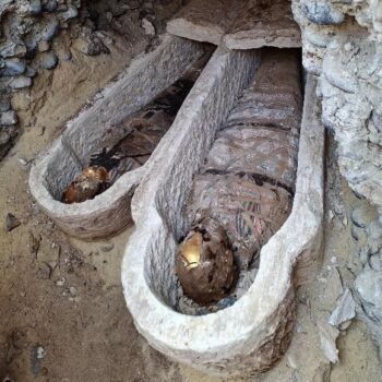 two wooden coffins with mummies inside wrapped in cloths with geometric shapes and with gold on the skulls