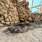 stone wall at left with blackish burned pile in front from wood burning
