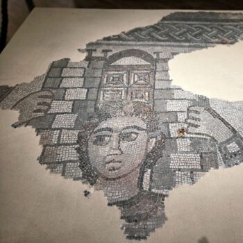 mosaic of samson with black curly hair and no beard with brickes behind him and gates above his head, arms raised. Courtesy Israel Antiquities Authority