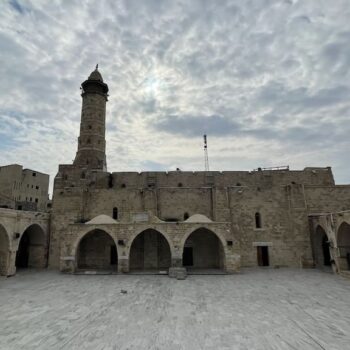The Omari Mosque in Gaza prior to its damage by 2023 airstrikes. Image shows a courtyard surrounded by arches, with a small tower in the background. Credit: Mounir Kleibo via Wikimedia Commons