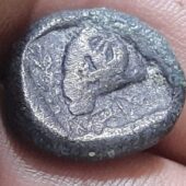 silver coin with a rim resting on two fingers, the coin's face has a triangular object that is a reported ram. Courtesy Israel Antiquities Authority