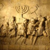 Image sculpted in relief upon stone archway of a menorah and other temple goods being carried off from the second temple by roman soldiers. Credit: Steerpike, via Wikimedia Commons, CC BY 3.0 Unported.