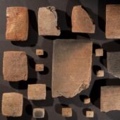 17 or so rectangular clay cuneiform tablets of various sizes, some large and some quite small, arranged on a gray floor. Courtesy Turkish Ministry of Culture and Tourism.